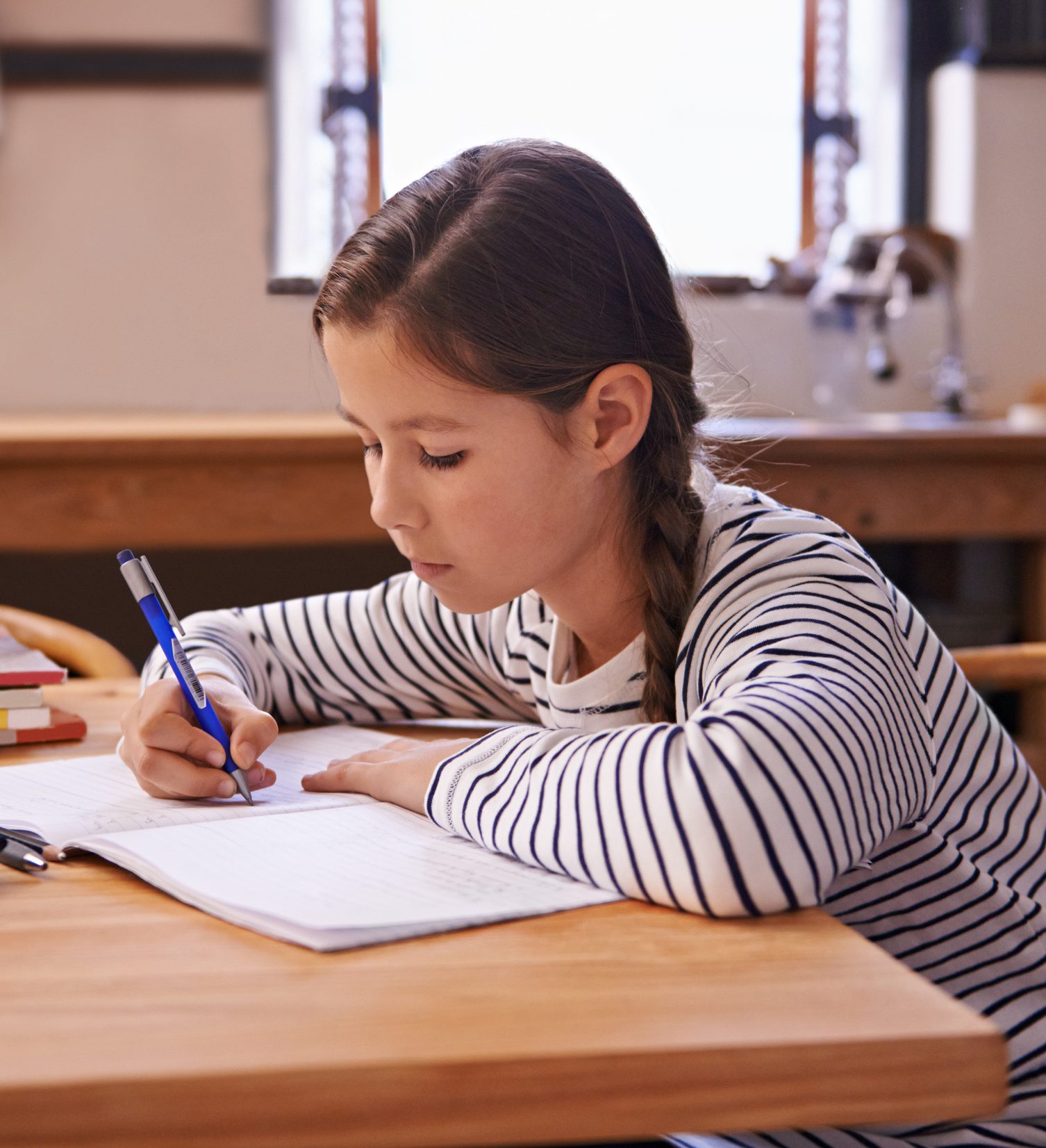 Middle school girl at kitchen table writing.