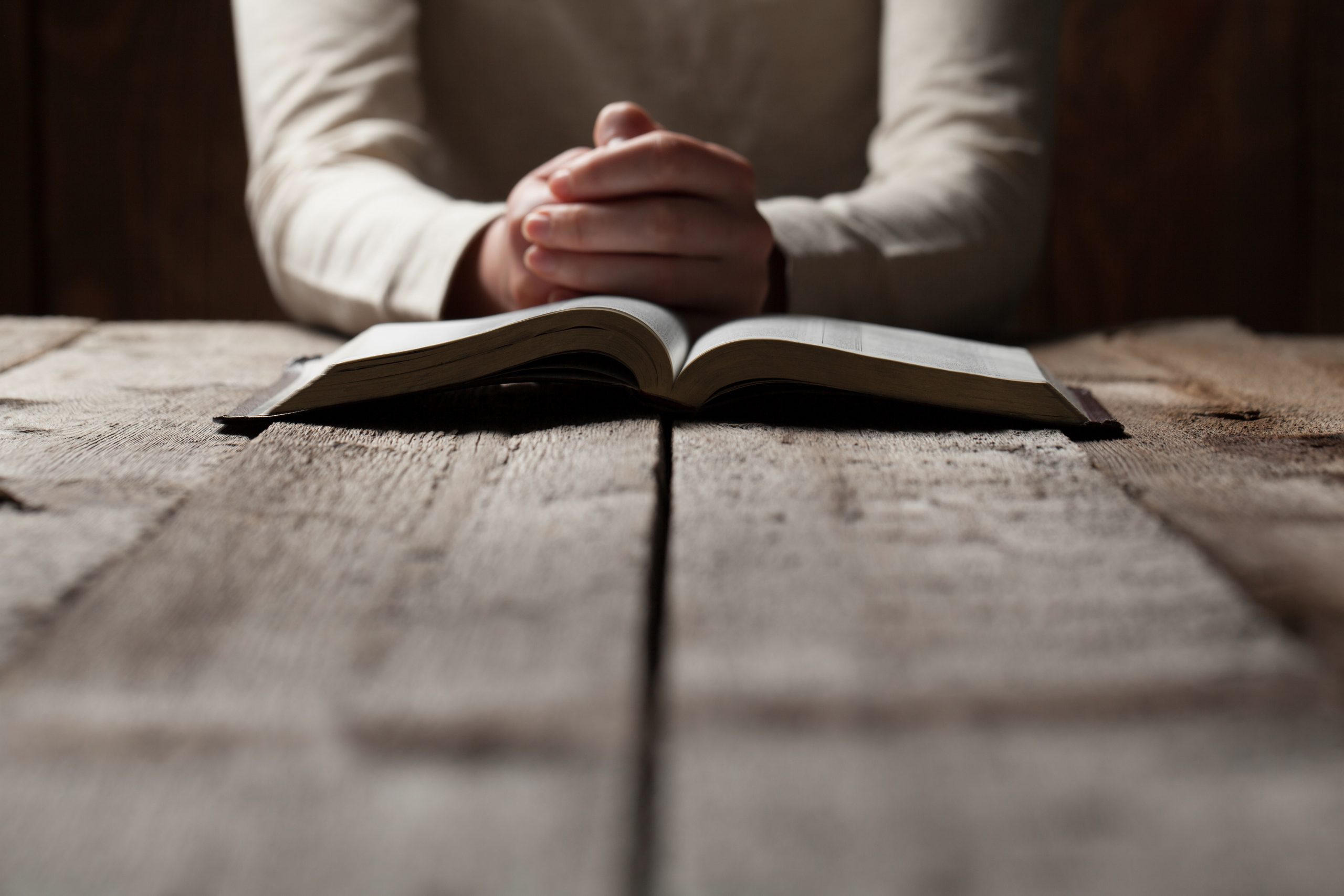 Woman hands praying with a bible at a wooden table